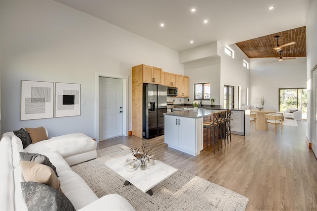 living room with ceiling fan, wood ceiling, a high ceiling, and light wood-type flooring