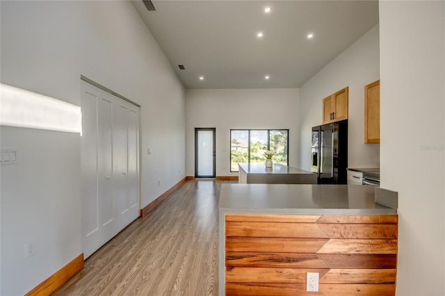 kitchen with light brown cabinets, a towering ceiling, light hardwood / wood-style floors, and black refrigerator with ice dispenser