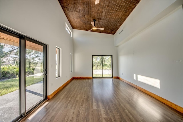 empty room with ceiling fan, a towering ceiling, wood ceiling, and wood-type flooring