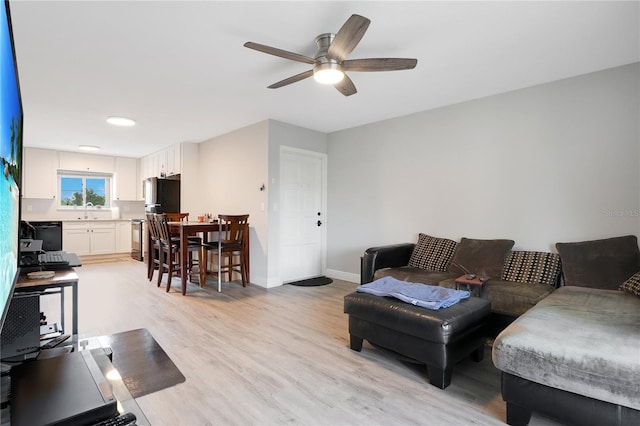 living area with baseboards, a ceiling fan, and light wood-style floors