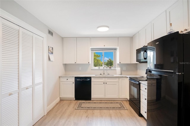 kitchen featuring light countertops, light wood finished floors, a sink, and black appliances