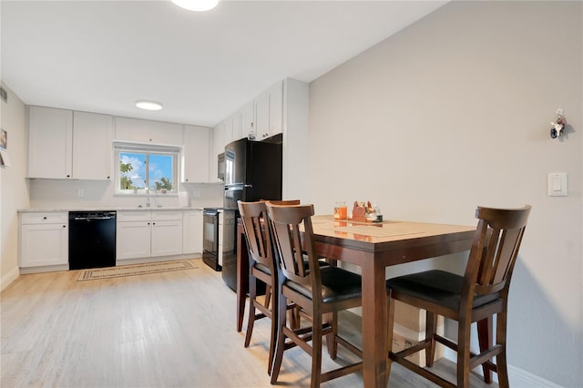 kitchen featuring a sink, black appliances, light wood-style flooring, light countertops, and white cabinetry