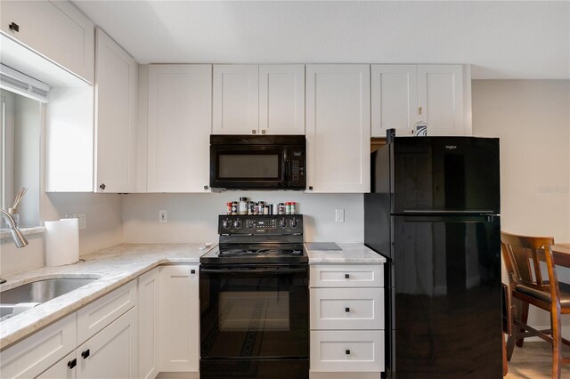 kitchen with hardwood / wood-style floors, sink, light stone countertops, black appliances, and white cabinetry