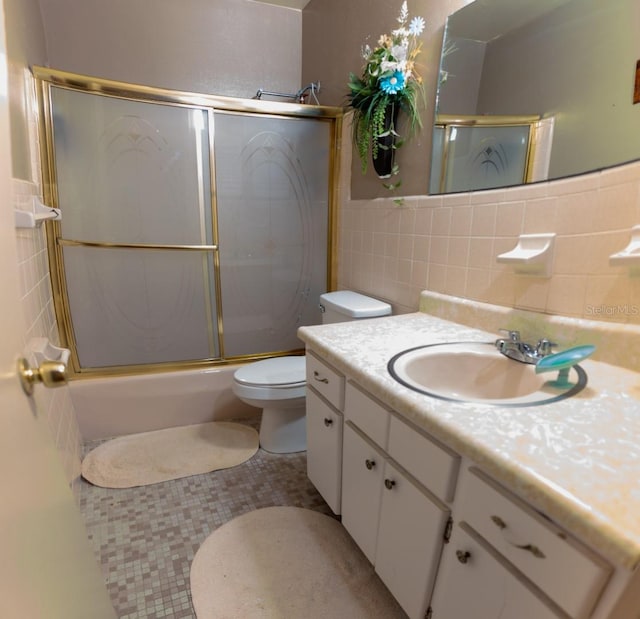 full bathroom with vanity, bath / shower combo with glass door, tile patterned floors, tile walls, and toilet