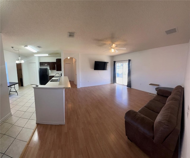 living room with ceiling fan with notable chandelier, light hardwood / wood-style flooring, a textured ceiling, and sink