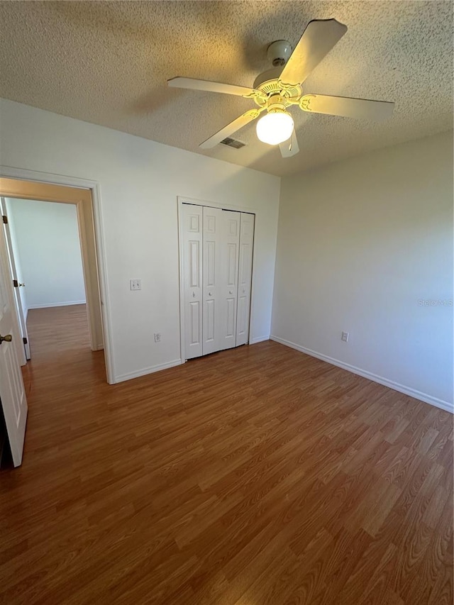 unfurnished bedroom featuring wood-type flooring, a closet, a textured ceiling, and ceiling fan