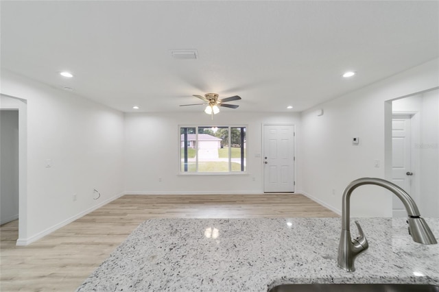 kitchen with light stone countertops, sink, light hardwood / wood-style flooring, and ceiling fan