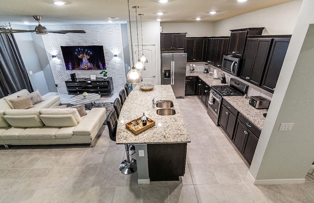 kitchen with ceiling fan, stainless steel appliances, decorative light fixtures, a breakfast bar area, and a center island with sink