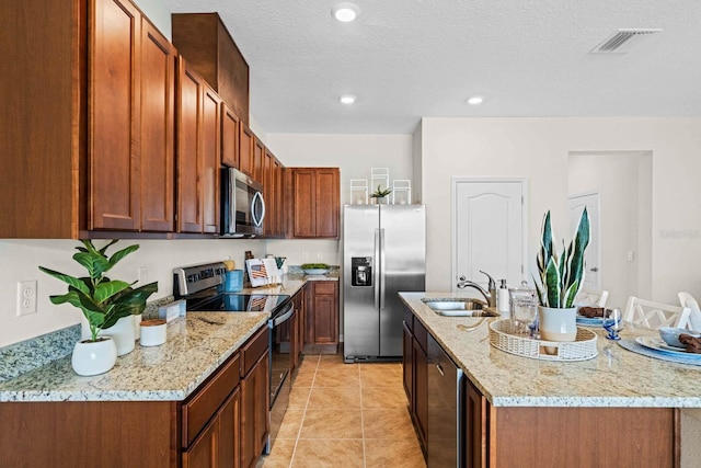 kitchen with a center island with sink, sink, light stone counters, appliances with stainless steel finishes, and a textured ceiling