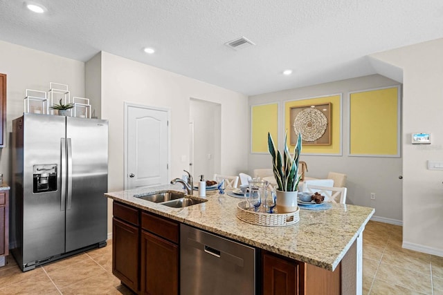 kitchen with light stone counters, stainless steel appliances, sink, a center island with sink, and a textured ceiling