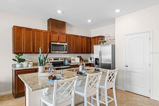 kitchen featuring light stone counters, sink, appliances with stainless steel finishes, a center island with sink, and a kitchen breakfast bar