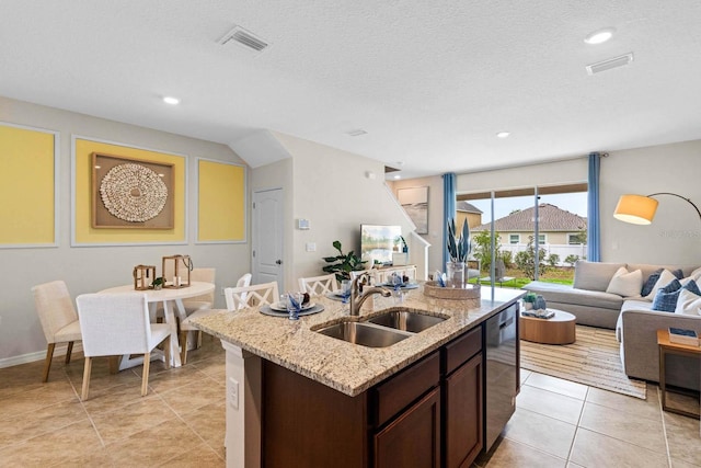 kitchen with sink, stainless steel dishwasher, dark brown cabinets, a center island with sink, and light stone countertops