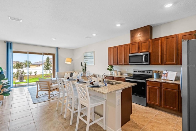 kitchen with sink, a textured ceiling, a kitchen island with sink, appliances with stainless steel finishes, and a breakfast bar