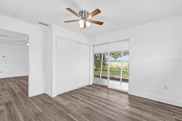 unfurnished bedroom featuring access to outside, a closet, dark wood-type flooring, and ceiling fan