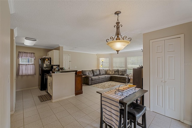 kitchen with black fridge, pendant lighting, light tile patterned floors, ornamental molding, and white cabinetry