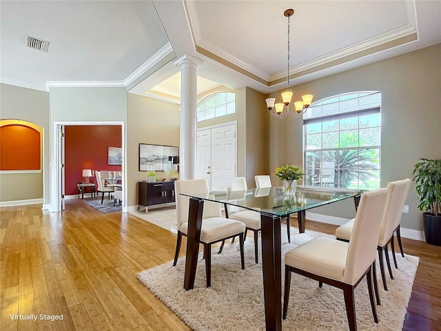 dining room with light hardwood / wood-style floors, a notable chandelier, ornamental molding, and decorative columns