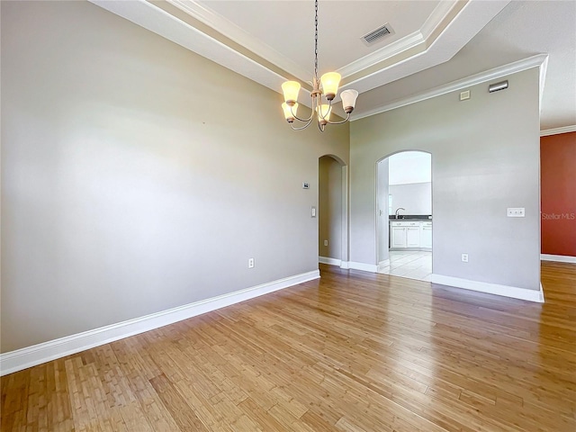 spare room featuring sink, light wood-type flooring, a tray ceiling, a notable chandelier, and ornamental molding