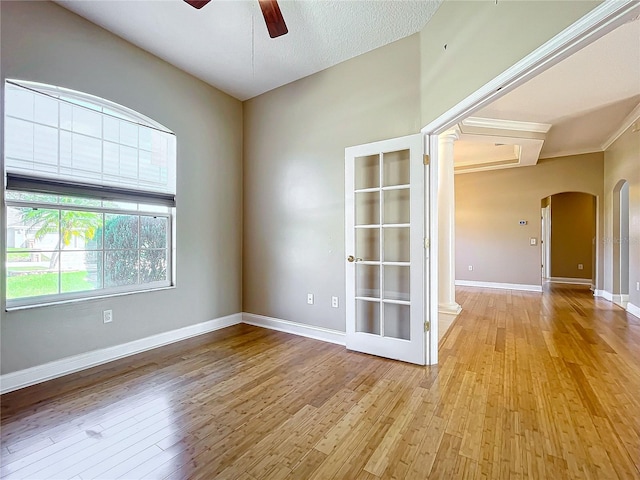 spare room featuring a textured ceiling, ornate columns, light hardwood / wood-style floors, ceiling fan, and crown molding