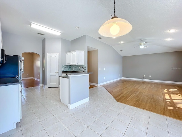 kitchen with light wood-type flooring, black fridge, ceiling fan, vaulted ceiling, and white cabinets