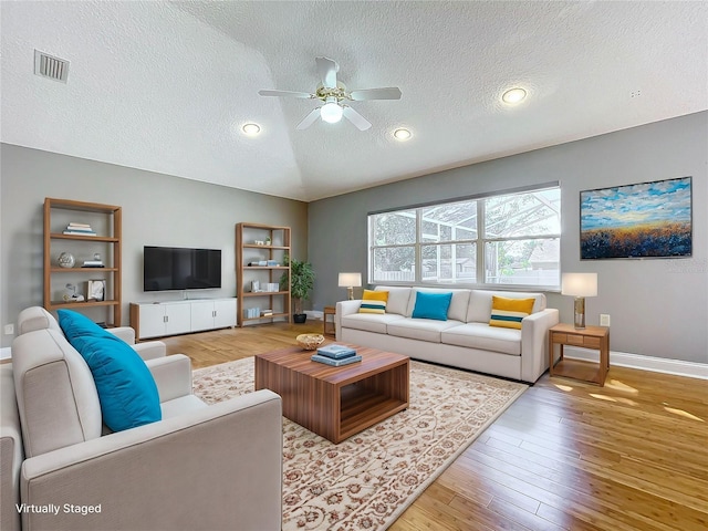 living room featuring light hardwood / wood-style floors, a textured ceiling, vaulted ceiling, and ceiling fan