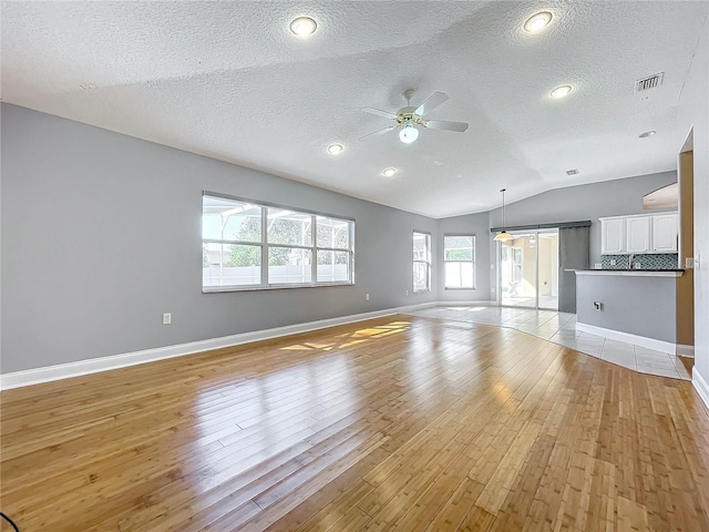 unfurnished living room featuring a textured ceiling, lofted ceiling, light hardwood / wood-style flooring, and a barn door