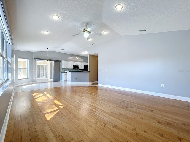 unfurnished living room featuring lofted ceiling, a textured ceiling, light hardwood / wood-style floors, and ceiling fan