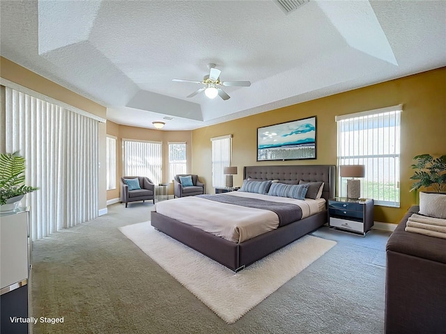 carpeted bedroom featuring ceiling fan, multiple windows, a textured ceiling, and a tray ceiling