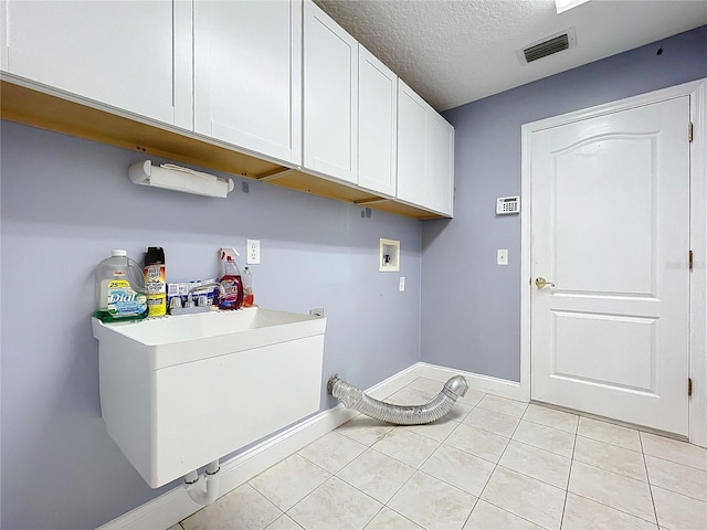 clothes washing area featuring cabinets, a textured ceiling, washer hookup, and light tile patterned floors