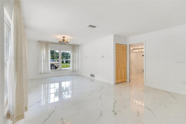 empty room featuring a textured ceiling and an inviting chandelier