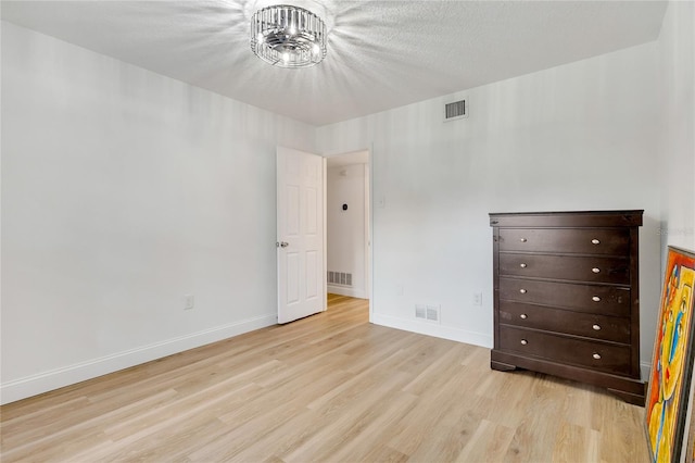 unfurnished bedroom featuring a notable chandelier, a textured ceiling, and light hardwood / wood-style floors