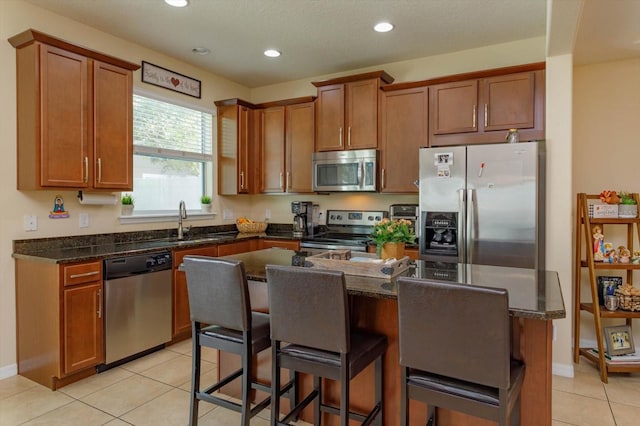 kitchen with appliances with stainless steel finishes, sink, a kitchen bar, a kitchen island, and light tile patterned floors