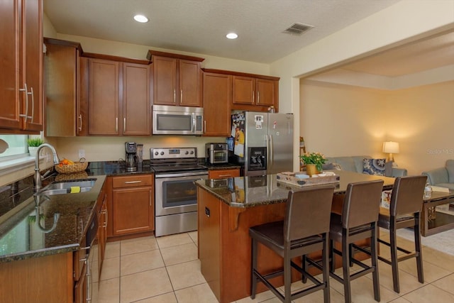 kitchen with stainless steel appliances, dark stone countertops, sink, a center island, and light tile patterned floors