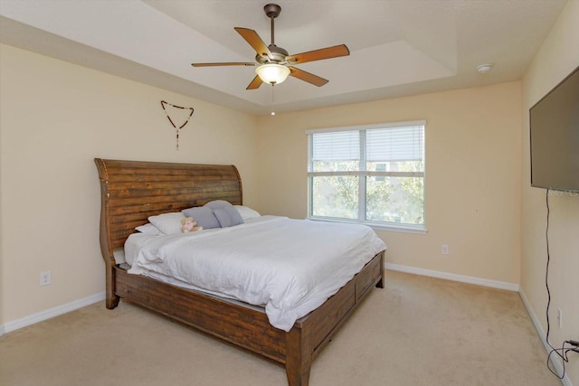 carpeted bedroom with a raised ceiling and ceiling fan