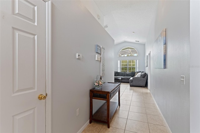 hallway with light tile patterned flooring, vaulted ceiling, and a textured ceiling