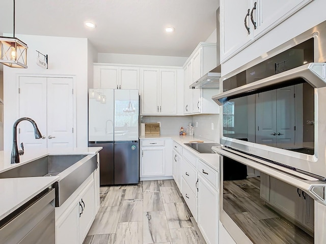 kitchen featuring white cabinetry, sink, hanging light fixtures, wall chimney range hood, and appliances with stainless steel finishes