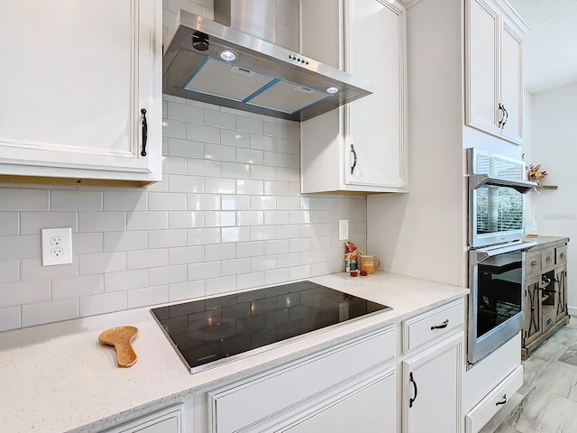 kitchen with ventilation hood, black electric stovetop, white cabinets, double oven, and tasteful backsplash