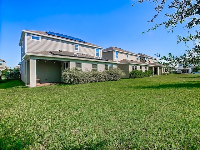 back of property with solar panels and a yard