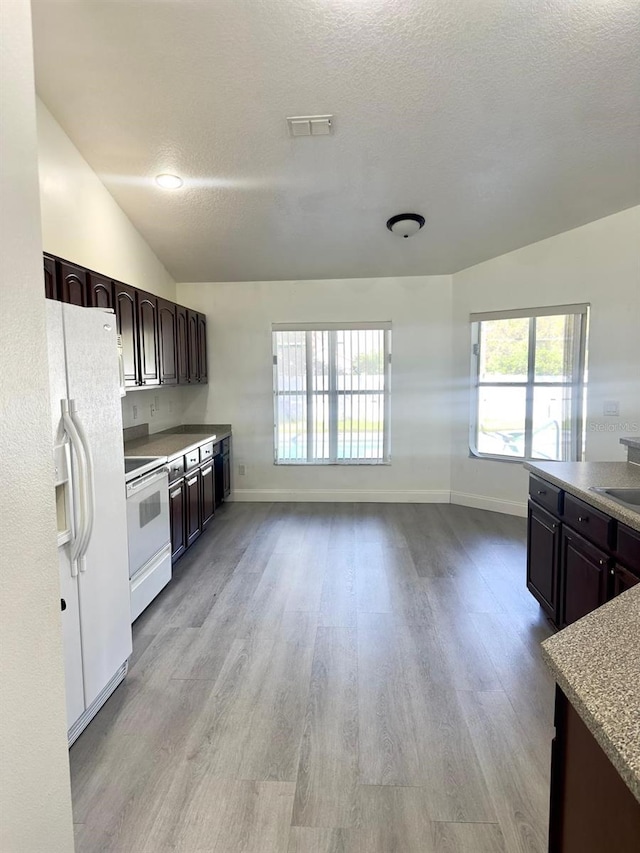 kitchen with dark brown cabinetry, vaulted ceiling, a textured ceiling, white appliances, and light wood-type flooring