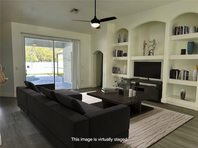 living room featuring built in shelves, ceiling fan, and dark wood-type flooring