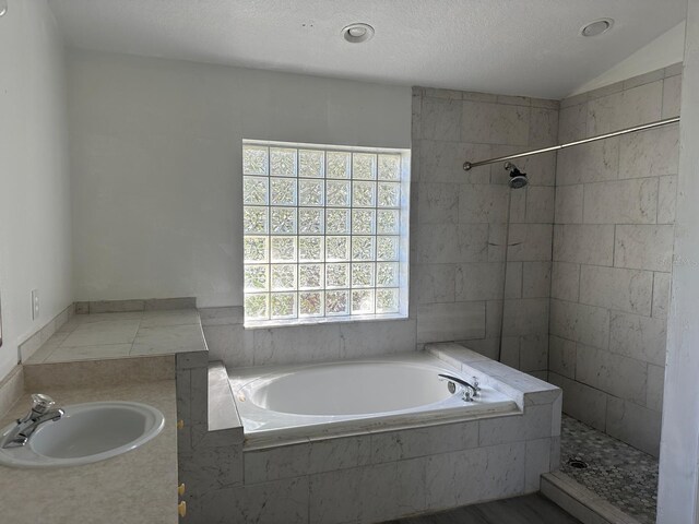 bathroom featuring shower with separate bathtub, a textured ceiling, lofted ceiling, and sink