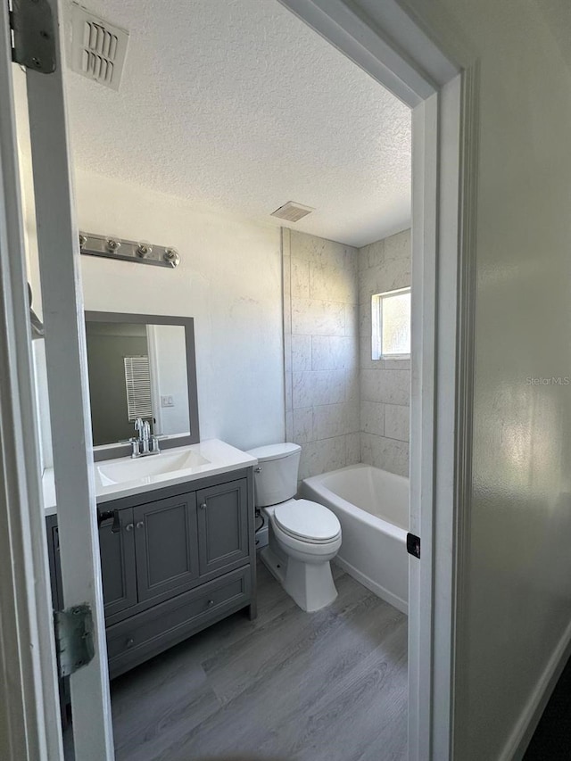 full bathroom with a textured ceiling, vanity, tiled shower / bath combo, hardwood / wood-style flooring, and toilet