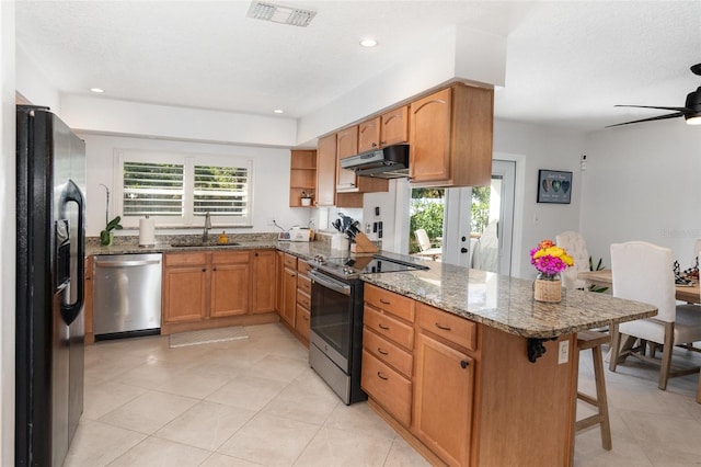 kitchen with stone counters, sink, kitchen peninsula, a breakfast bar area, and appliances with stainless steel finishes