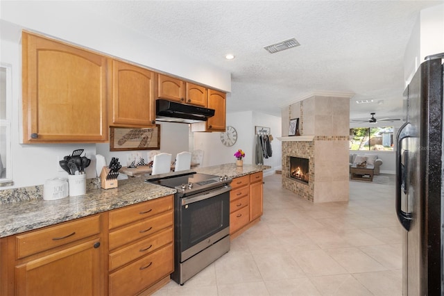 kitchen featuring stainless steel electric range, black fridge, a brick fireplace, ceiling fan, and a textured ceiling