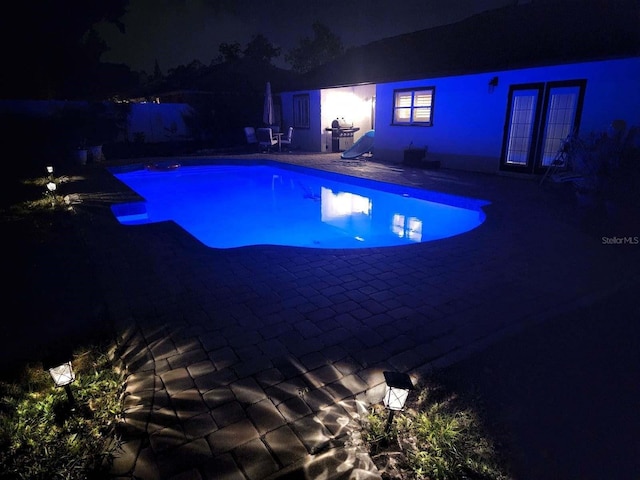 pool at night featuring french doors and a patio