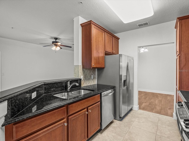 kitchen featuring dark stone counters, a textured ceiling, stainless steel appliances, sink, and light tile patterned floors