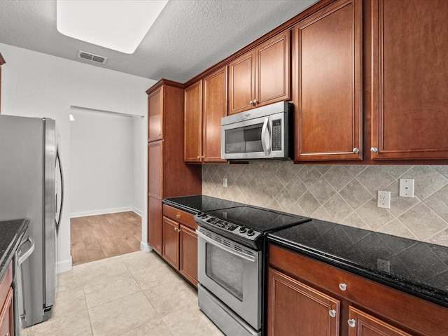 kitchen with appliances with stainless steel finishes, backsplash, light tile patterned floors, and dark stone counters