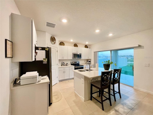 kitchen with white cabinetry, a breakfast bar, a center island with sink, stainless steel appliances, and a textured ceiling