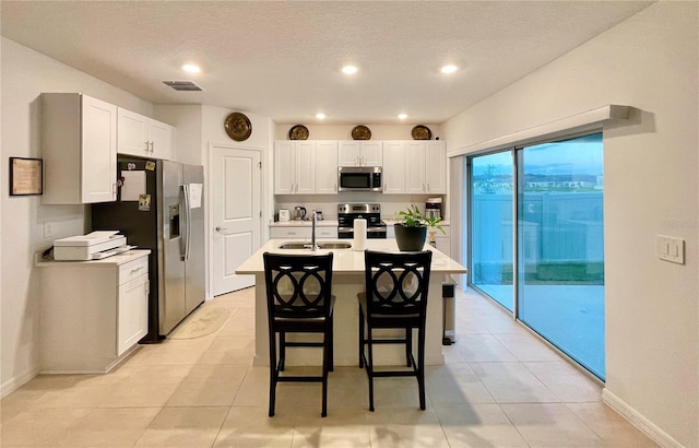 kitchen with sink, white cabinetry, a breakfast bar area, appliances with stainless steel finishes, and a center island with sink