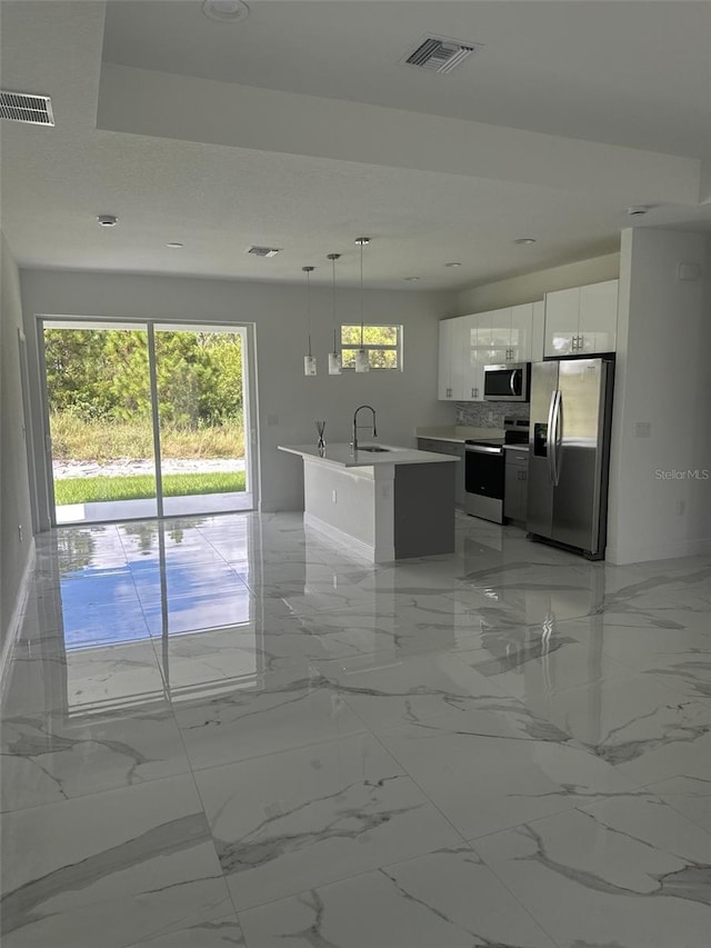 kitchen featuring a kitchen island with sink, stainless steel appliances, sink, white cabinetry, and decorative light fixtures