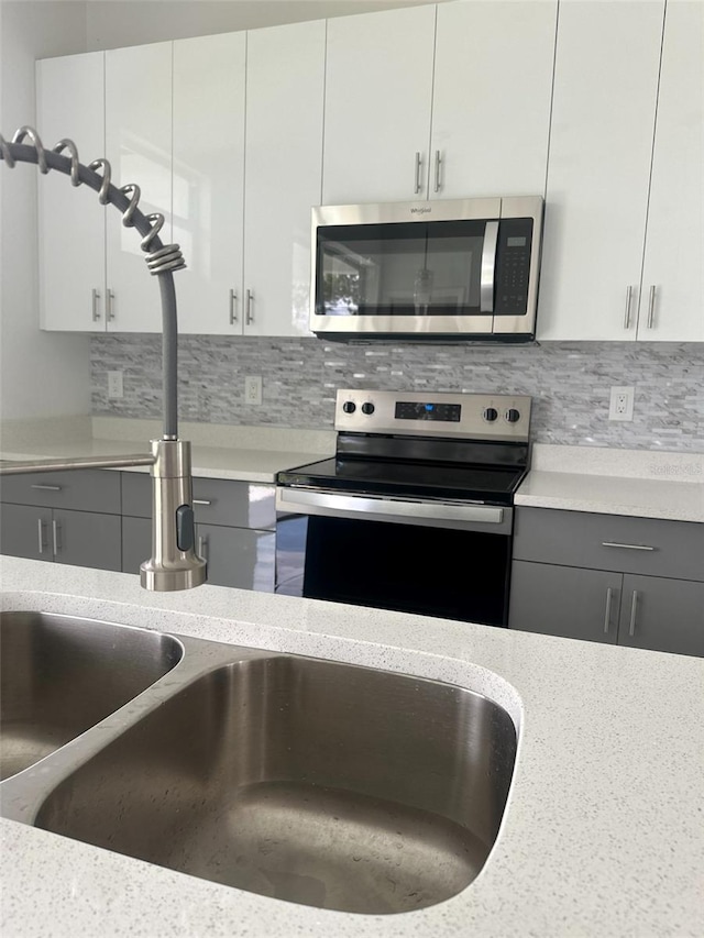 kitchen featuring decorative backsplash, sink, light stone counters, stainless steel appliances, and white cabinetry